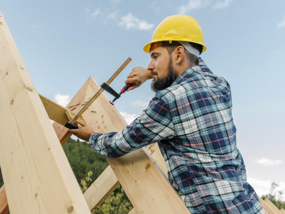 Handwerker mit Schutzhelm befestigt Holzbalken beim Bau eines Dachstuhls