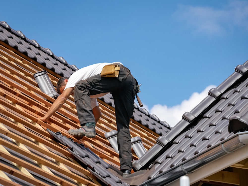 Handwerker arbeitet auf dem Dach und verlegt Dachziegel bei der Neueindeckung