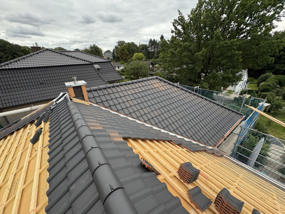 Bauarbeiten an einem Hausdach mit dunkler Dacheindeckung und sichtbarer Holzkonstruktion